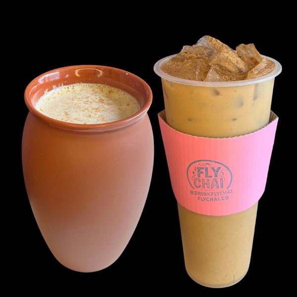 A terracotta-colored ceramic mug filled with a light beige beverage and a clear plastic cup with an iced coffee drink and a pink Fly Chai sleeve, set against a solid black background.