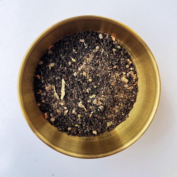 Brass bowl filled with dark tea leaves on a white background