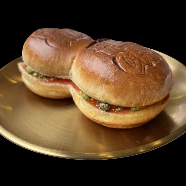 Two golden-brown sandwich buns filled with green chutney and red sauce, presented on a round gold plate against a solid black background.