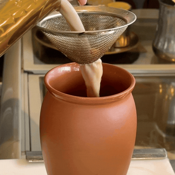 Close-up GIF of creamy masala chai being poured through a traditional metal strainer into a rustic clay Kulhad cup.