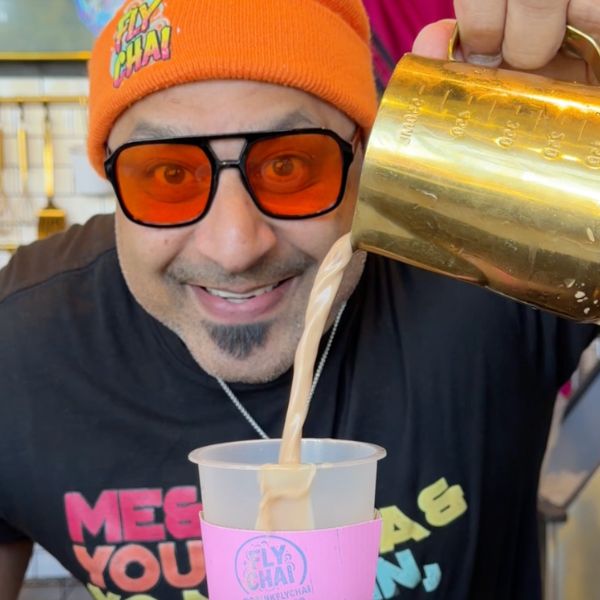 Person pouring a creamy beverage from a gold pitcher into a cup with a colorful label.